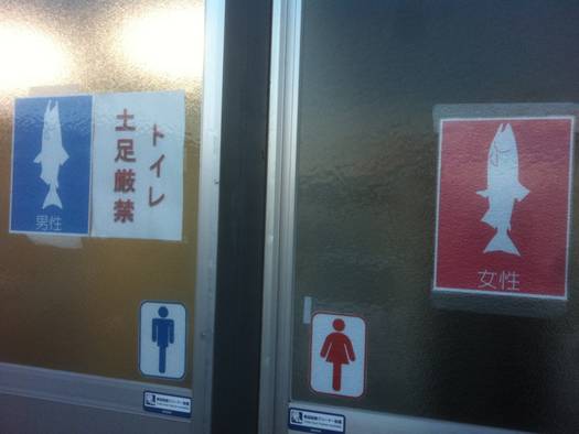 志津川魚市場のトイレの入り口に、青と赤のさけのイラストで男女を示す表示がされている様子の写真