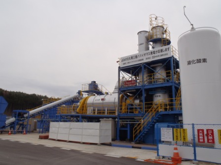 液体窒素と書かれた大きなタンクの隣に、青い鉄骨の建物があり、大小のタンクや配管が見えるバイオマス発電設備の写真