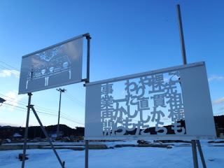 雪の積もった地面の上に、物を形どったきりこの看板と、文字が切り抜かれたきりこの看板を写した写真