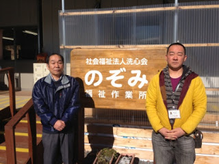 社会福祉法人洗心会のぞみ福祉作業所の看板の前に立つ畠山所長と森さんの写真