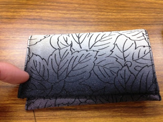 黒とグレーの葉柄の布地で丁寧に作られた名刺入れが置かれており、左端から指で作品を指して紹介しているような構図の写真
