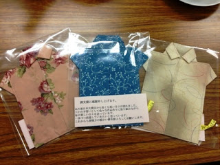 色柄の異なる布で仕立てたシャツ型のポケットティッシュケースが三つ透明な袋に入れられて並べられており、中央には震災支援への感謝の言葉が書かれた紙が添えられている写真