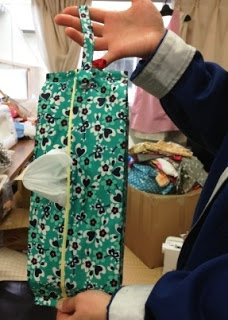 緑地に黒と白の花柄の布で作られた吊るせるティッシュケースを手で持ち上げて見せている写真