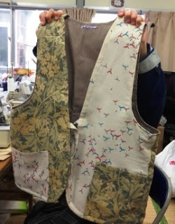 異なる柄の布を組み合わせて手作りされたベストを両手で持っている様子の写真