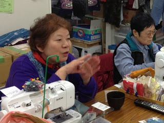 ミシンの置かれた作業場で話をしている三浦幸子さんの写真