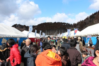 のぼりを立てた白いテントが、左右に立ち並び、その間の通路を大勢の来場者が行きかっている、混雑した会場の写真
