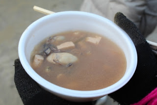 白いプラスチックの器に牡蠣、豆腐、その他の具材が入っている牡蠣鍋を写した写真