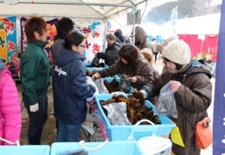 屋外のテントの下で数人が青い容器に入っためかぶを袋に詰めているめかぶ詰め放題の写真