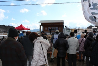 トラックの荷台のステージの周りに多くの人々があつまっている賑わいの様子を写した写真