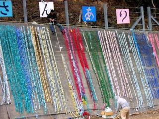 高い塀に一人が昇り、一人は塀の下で、折り鶴の簾を下げる作業を行っている様子を写した写真