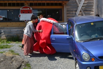 青い軽自動車の後部座席に、大きなオクトパスの着ぐるみを協力して乗せようとしている写真