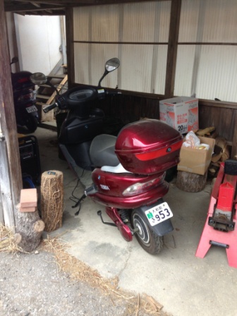 屋根付きの木造の小屋の中に停められている赤いバイクの写真