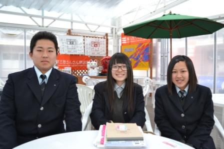 制服を着た高校生の男女3人が白い丸テーブルを囲んでにこやかに座っている写真