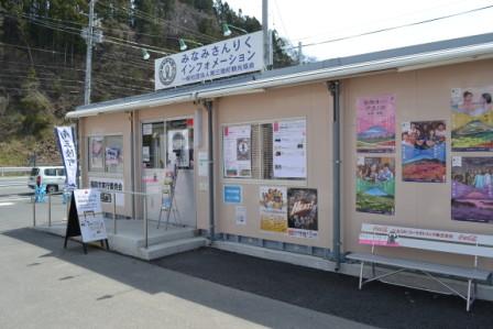 みなみさんりくインフォメーション」と書かれた看板が掲げられた仮設型の観光案内所が写っており、入口のそばには観光パンフレットが置かれ、建物の外壁には地域イベントや観光地を紹介する多数のポスターが貼られている写真