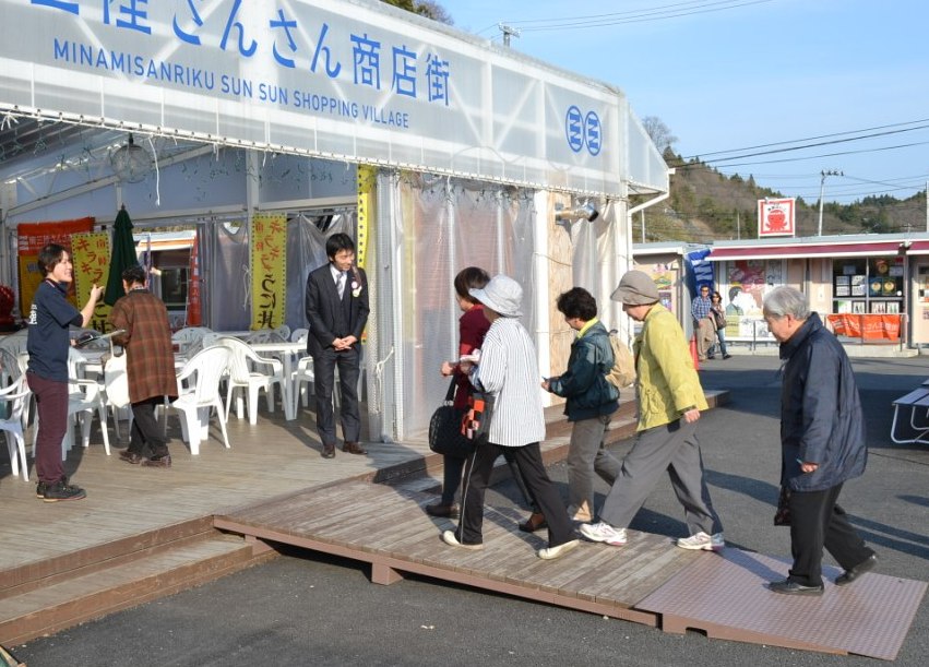 白いビニールテントでできた「南三陸さんさん商店街」の建物に次々とツアーの参加者が入っている写真