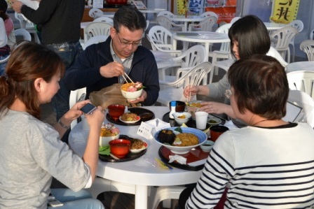 4人の男女が白い丸テーブルを囲み、食事を楽しんている様子の写真