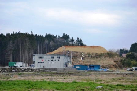 避難道を整備している山とその下に建っている工場を遠目から写した写真