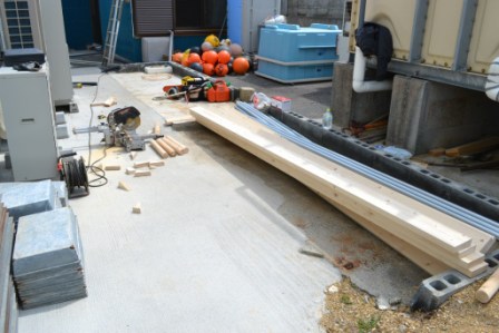 電動のこぎりや長い板の木材、などが置かれた作業場を写した写真