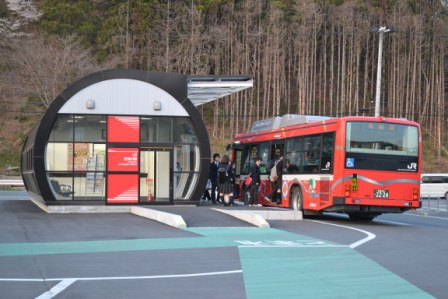 屋根付きのバス停で学生が並んで停車したバスに乗り込もうとしている写真
