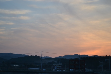 夕暮れの空が赤く染まり山々の稜線がシルエットのように浮かび上がり、その手前に建物が並んでいる写真