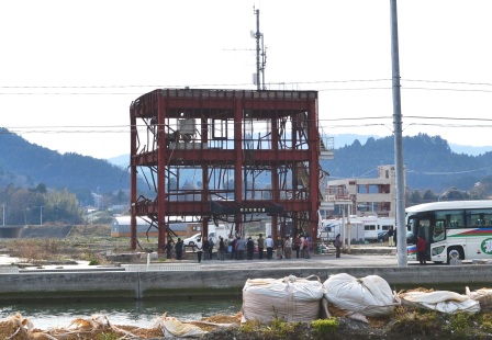 鉄骨だけになった3階建ての防災庁舎をバスで訪れる人々の写真