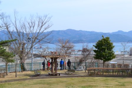 海に面した公園で、数人の人々が柵のそばに立って町の様子を見学している写真