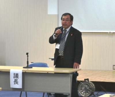 議長の及川善祐さんが議長席の横に立ち、マイクをもって挨拶をしている様子の写真