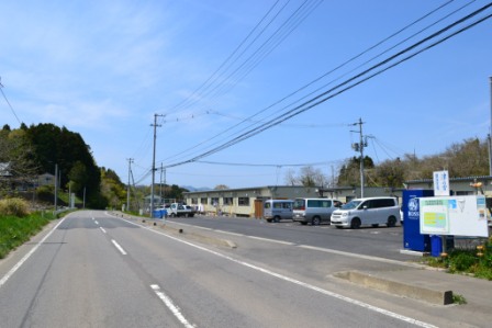 道路沿いに駐車場があり、その奥に仮設住宅が並んでいる写真