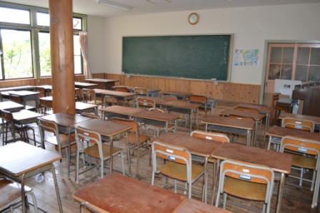 前方に黒板があり木製の机と椅子が整然と並べられている教室の写真