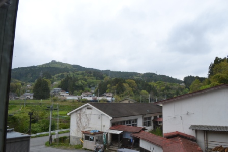 建物の窓から見える風景で、田舎の集落や緑の山々が広がっている様子の写真
