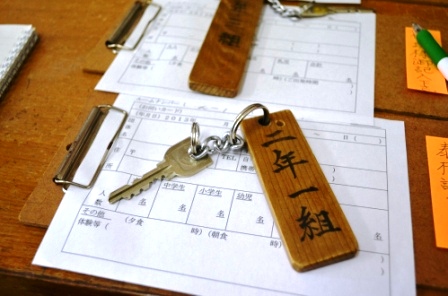 「二年一組」と書かれた木製キーホルダー付きの鍵が、宿泊者名簿のような紙の上に置かれている写真