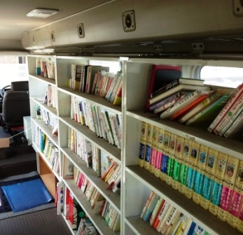 車内の右側に白い本棚が並び、多くの児童書や文庫本が並んでいる様子を写した写真