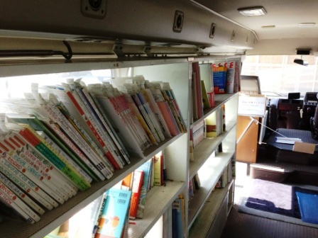 移動図書館の車内には壁に沿って白い本棚が設置されており、絵本や児童書と思われるたくさんの本が棚に並んでいる様子の写真
