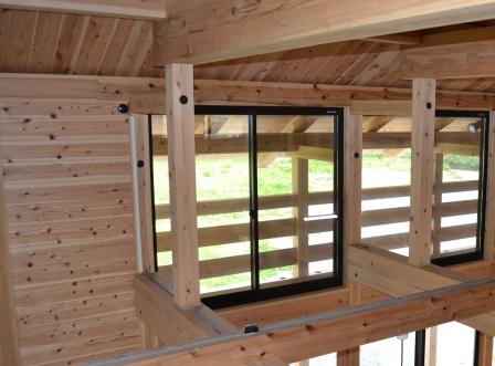 建物の2階からバルコニー側を見下ろした視点で、柱や手すり、壁や天井など全体が木材で統一されている室内の様子の写真