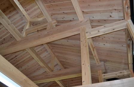建物の内部から見上げた天井部分で、梁や垂木が複雑に組み合わされ、全体が杉のような木材で美しく仕上げられている屋根裏構造の写真