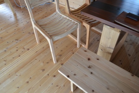 木の床の上に、同じく木で作られたテーブルや椅子が並べられ、シンプルで温かみのあるデザインの家具が調和している室内の写真