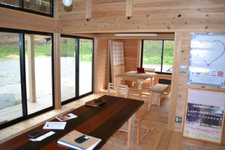 木の内装で統一された広々とした室内に、テーブルと椅子が配置され、自然光が大きな窓から差し込んでいる温もりのある空間の写真