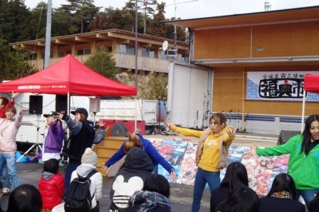 屋外のステージ前で数人の若者がダンスパフォーマンスを披露しており、観客がステージ前に並んでダンスを見ている様子を写した写真