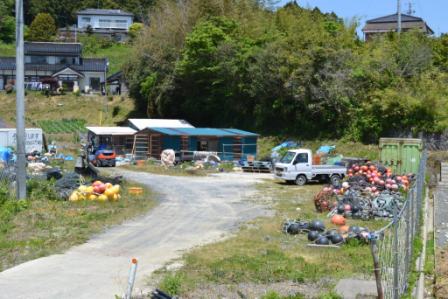 木造の小屋のそばに白いトラックが停まっていて、浮き玉が山のように置かれた写真