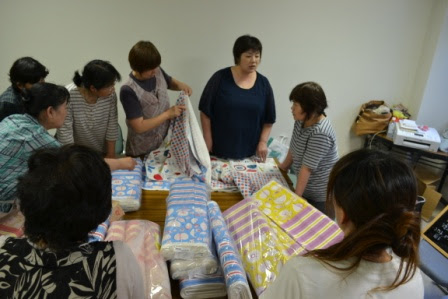 大きなテーブルの上にたくさんのカラフルな布が並び、複数の女性たちが布を手に取りながら話をしている写真