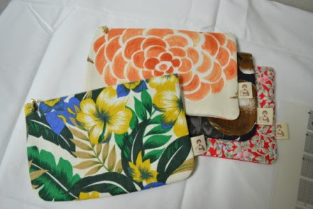 花や葉の模様が描かれたファスナー付きの布製ポーチが4つ、白い布の上に重ねて置かれている写真
