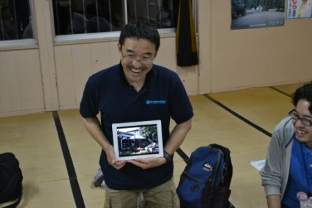 紺色のシャツを着た男性が写真をもって発表をしている様子の写真