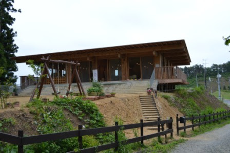 木造平屋建ての園舎が正面から見え、建物前には植栽と子ども用のブランコがあり、ゆるやかな階段が園舎へと続いている写真