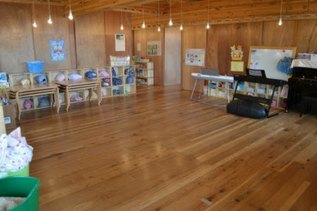 木の壁と床に囲まれた教室内に、お道具類が入った棚、ピアノ、キーボード、季節の飾りが掲示されている室内の写真