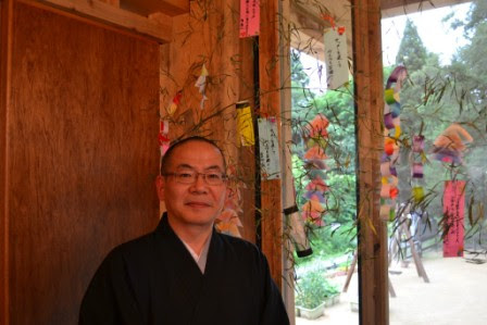 七夕祭りの前に立つ、黒い和服姿の小島孝尋園長先生の写真