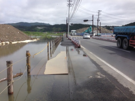 道路脇の歩道が冠水しており、歩けるようにベニヤ板が水面に敷かれている写真