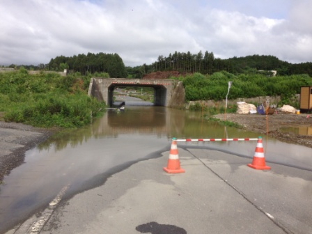 小さなコンクリートのトンネルの手前の道路が大きく冠水しており、進入禁止のパイロンが立っている写真
