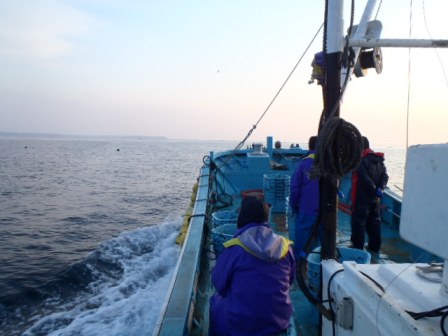 走り出した漁船の上で作業員たちが準備を進める様子を船尾側から撮影した写真