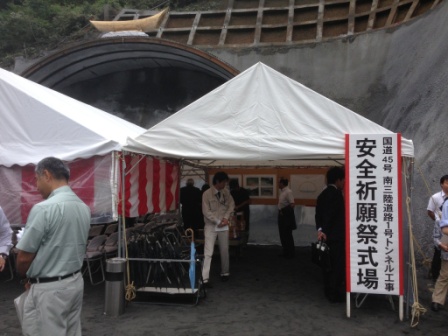清水トンネル入口前に設置された白いテントに「国道45号南三陸道路清水トンネル工事 安全祈願祭式場」と書かれた立て看板が立っており、作業員や関係者が集まっている、安全祈願祭会場の写真
