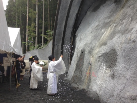 神職がトンネル坑口の岩盤に向かって白い紙吹雪を撒き、安全を祈願する神事を行っている、安全祈願の清祓いの写真